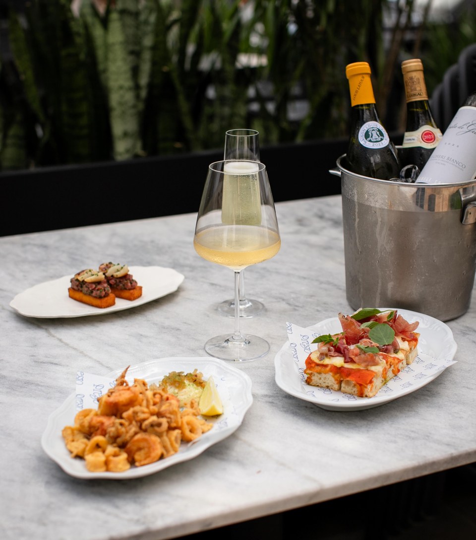 Mesa de mármore com taça de vinho branco no balde, fritto di mare e bruschettas para dividir.