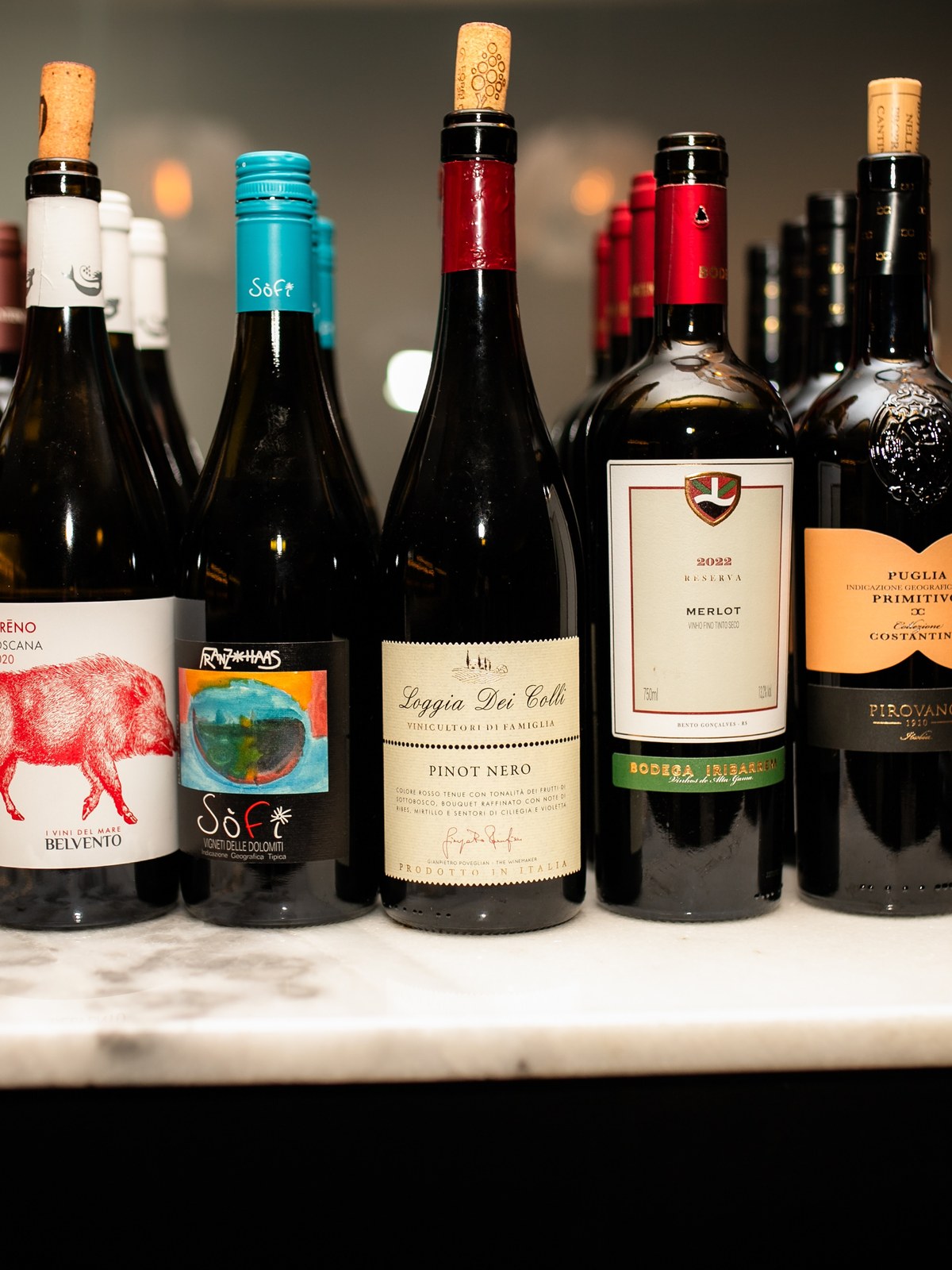 Fileira de garrafas de vinho italianas alinhadas no balcão de mármore.