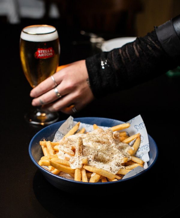 Cacio e Pepe Fries em tigela azul, cobertas de espuma de queijo e pimenta, ao lado de um chope.
