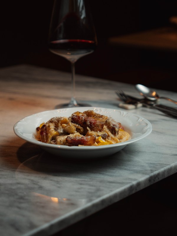 Carbonara de rigatoni servida em prato fundo branco.