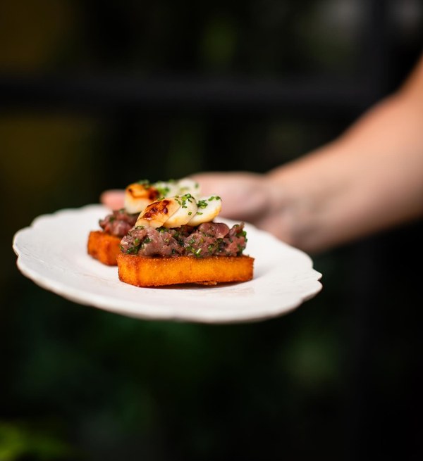 Crudo di Manzo con Capesante sobre crostini de polenta frita, servido na mão.